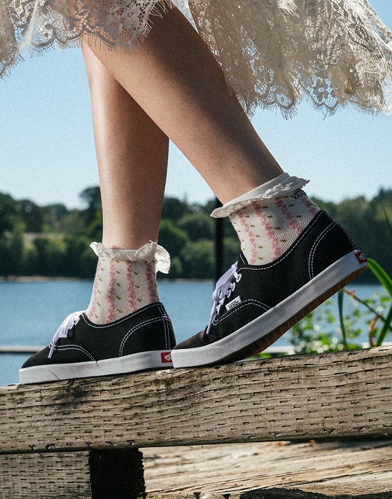 Someone walks on a wooden handrail wearing black and white Authentic paired with white frill socks.