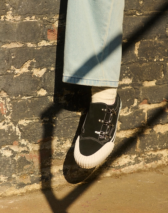 A close-up of someone wearing Karina Rozunko’s Premium Old Skool with Check-5 Baggy Denim Pants as they sit on a brick wall.