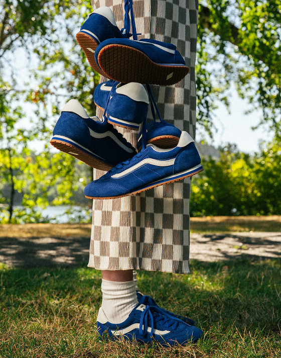 A waist-down shot of someone in a park wearing blue Super Lowpro shoes and holding three other pairs by their laces.