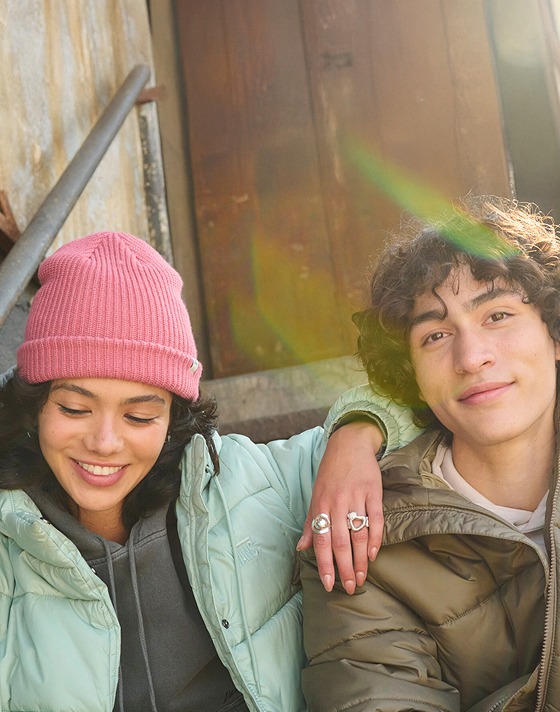 A young man and woman sit on the steps of a warehouse wearing MTE Hillgate Puffers.