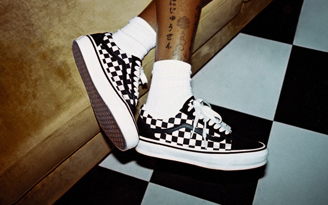 Close-up on a young man wearing black and white Checkerboard Old Skool on a leather sofa.