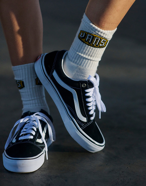 A close-up of someone wearing black and white Old Skool with white crew socks in a warehouse.