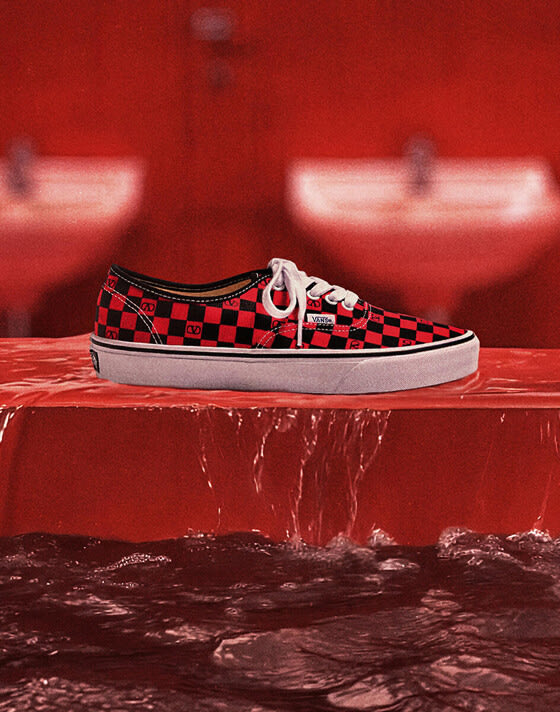 A close-up of the pink and black checkerboard pattern on the Authentic by Valentino Garavani and Vans in a red room.