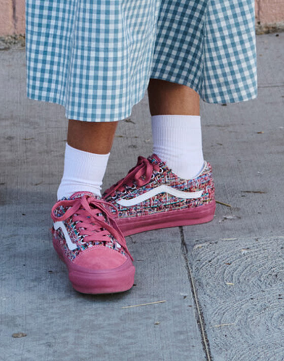 A close-up of pink tweed Premium Old Skool paired with white socks and a light blue gingham skirt on the sidewalk.