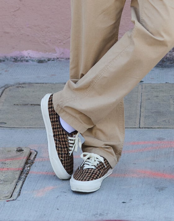 A knee-down shot of someone wearing up Premium Authentic Harris Tweed shoes with chinos on the sidewalk.
