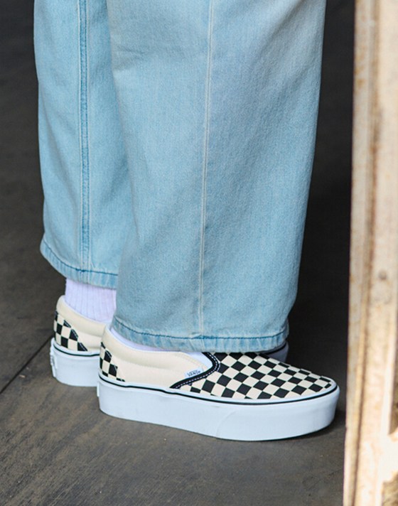 A waist-down shot of a woman wearing Classic Slip-On Checkerboard Platform shoes with Check-5 Baggy Denim Pants.