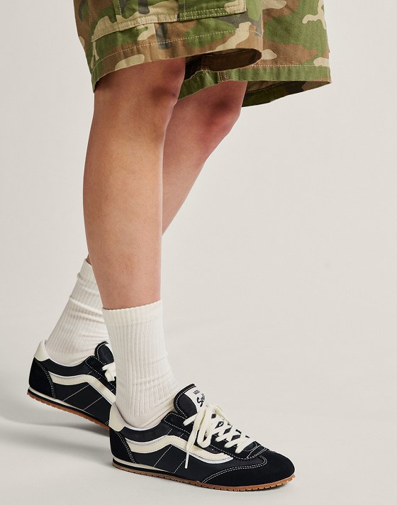 A knee-down shot of someone wearing black and white Super Lowpro with camo shorts in a photography studio.