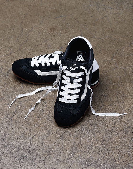 A pair of black and white Super Lowpro rest on the sidewalk with their laces undone.