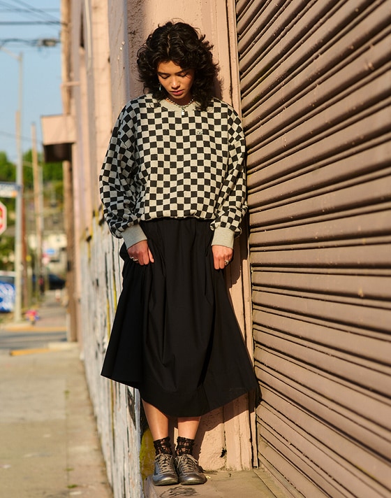 A young woman wearing a black Francesca Full Skirt and the Checkerboard Retro Crew Sweatshirt looks down at her gunmetal gray Super Lowpro.