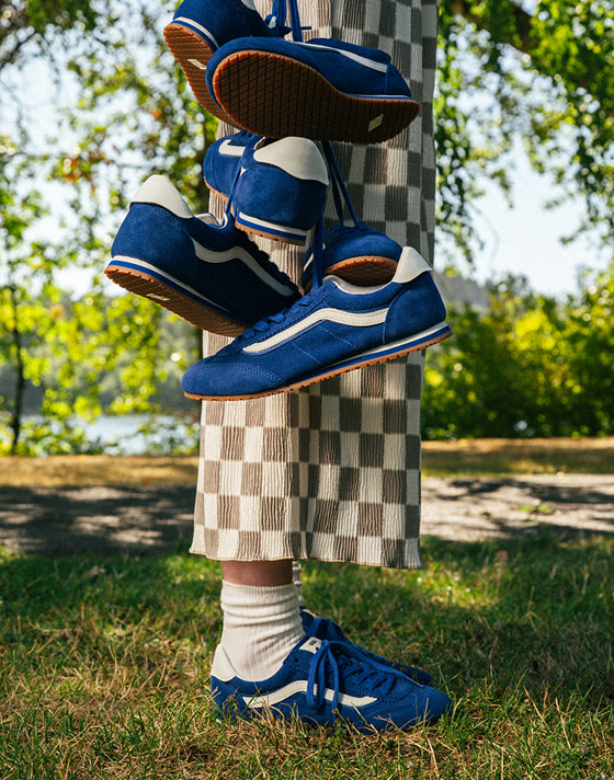A waist-down shot of someone in a park wearing blue Super Lowpro shoes and holding three other pairs by their laces.