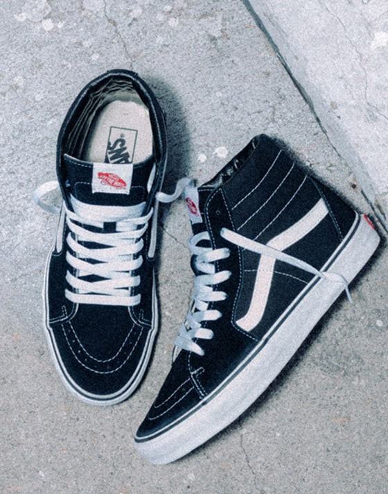 An overhead shot of black and white Sk8-Hi with their laces undone on the sidewalk.