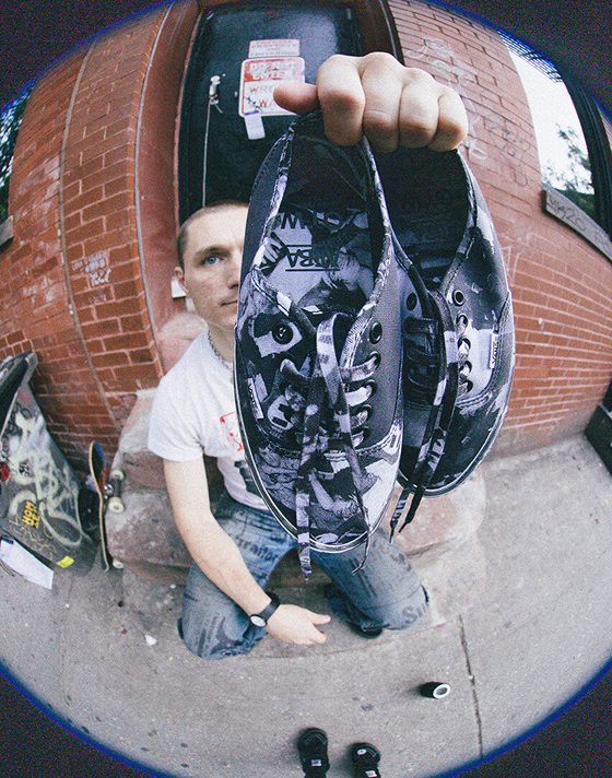 A fisheye shot of a skater holding up a pair of OTW Authentic 44 by Atiba Jefferson outside of a brick building.