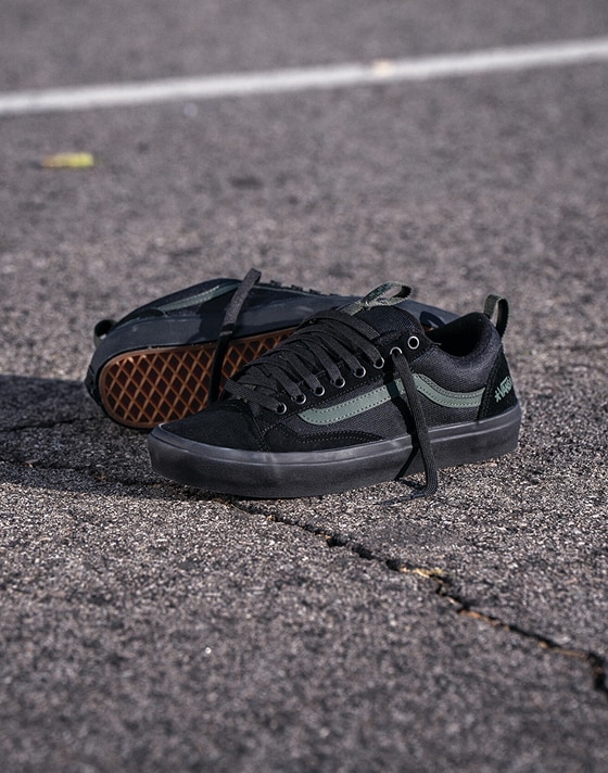 A pair of black Skate Old Skool 36+ from the United Through Skateboarding collection lie on the blacktop of a playground.