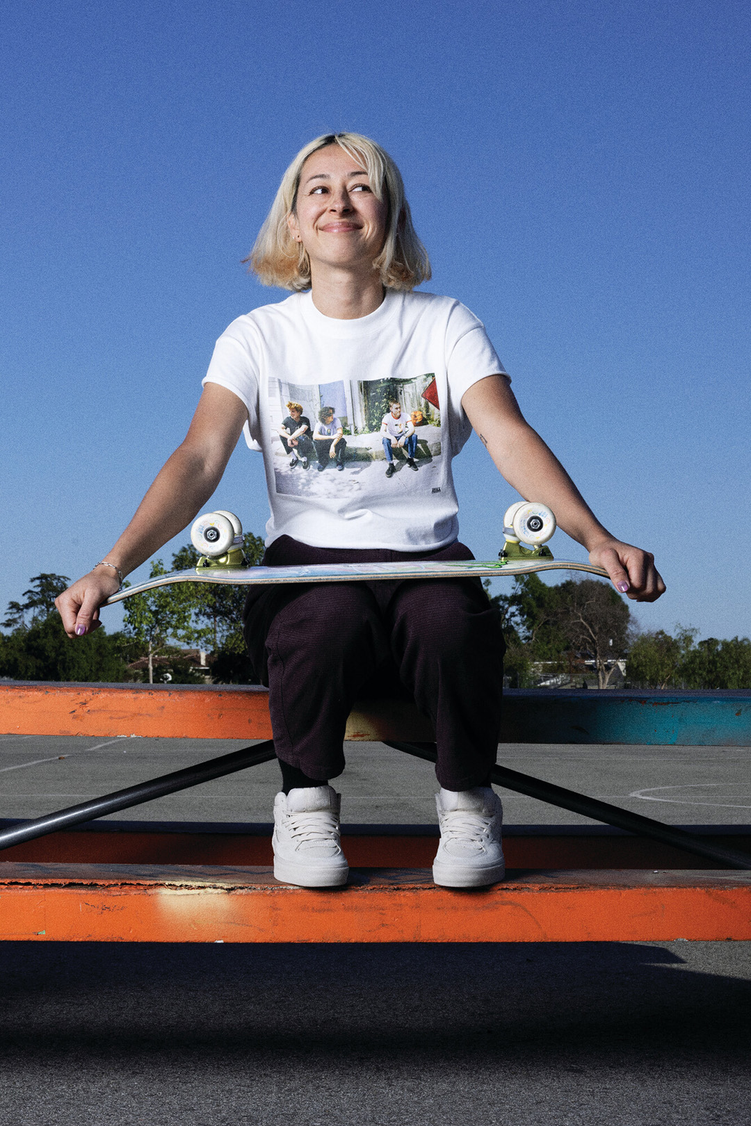 Lizzie Armanto sitting on a table holding a skateboard.