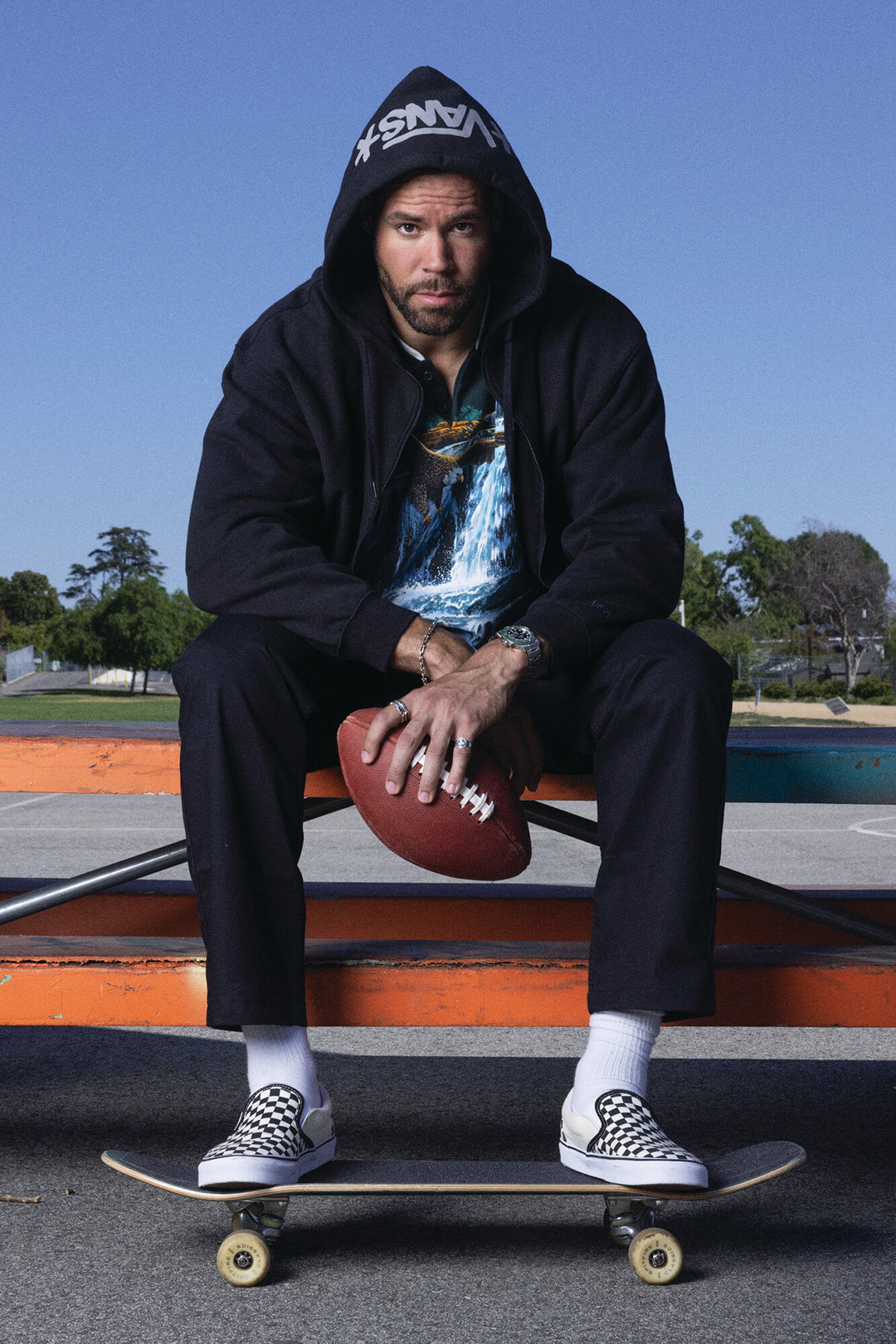 C.J. Uzomah sitting on table, football on hand, feet resting on a skateboard.