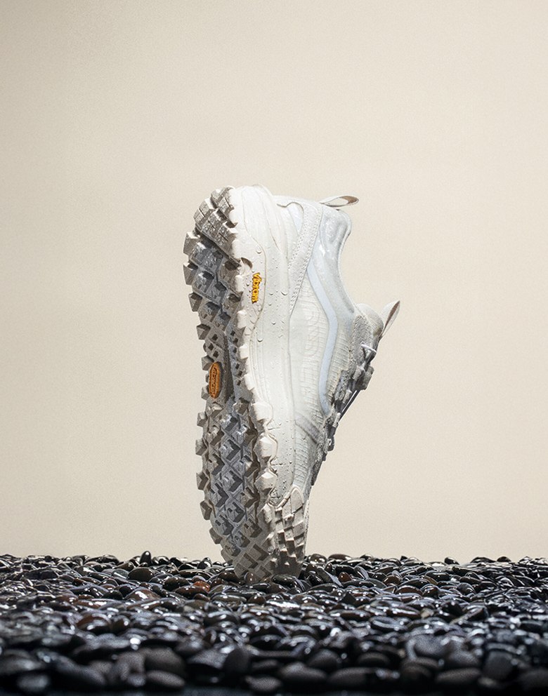 The white Crosspath XC GORE-TEX balancing on its toe vertically on top of black gravel with moisture on the shoe.