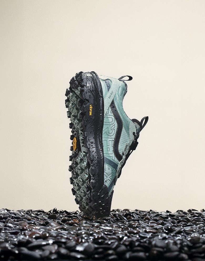 The blue Crosspath XC GORE-TEX balancing on its toe vertically on top of black gravel with moisture on the shoe.