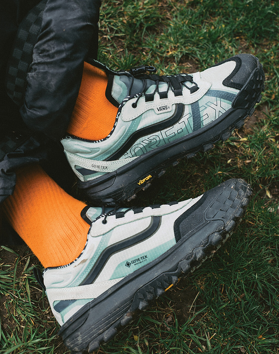 A close-up of someone wearing blue Crosspath XC GORE-TEX with black pants and orange socks on the grass.