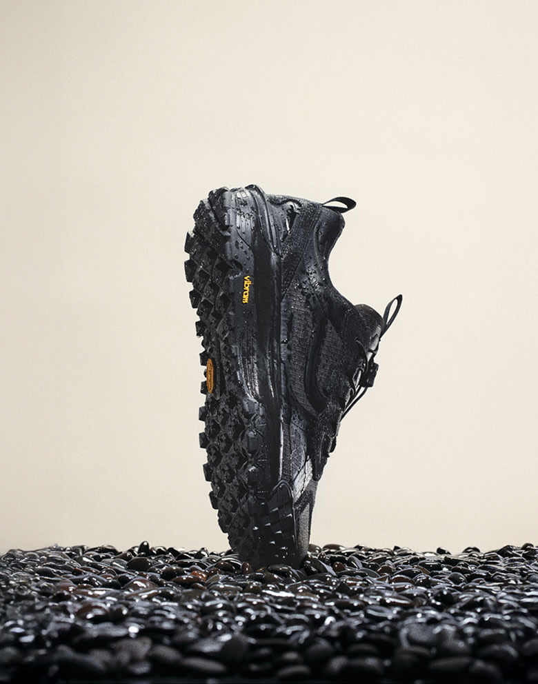 The black Crosspath XC GORE-TEX balancing on its toe vertically on top of black gravel with moisture on the shoe.