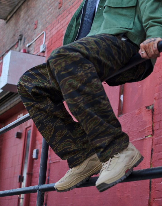 A man sits outside of a warehouse on a rail wearing MTE Sk8-Hi GORE-TEX Insulated boots and Skate Loose Atiba Haze Cargo pants.