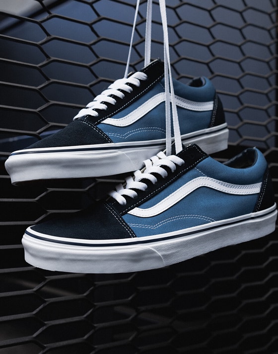 A pair of blue and black Old Skool hang from a gate in dim light for an urban ambiance.