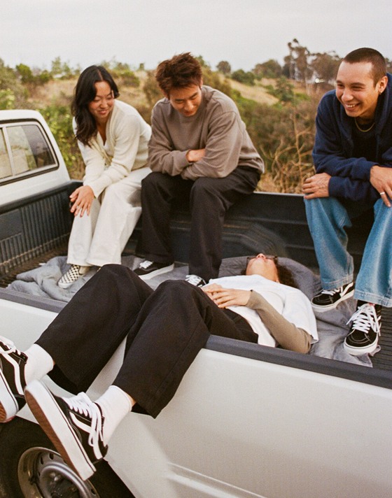 A group of friends hang out in the bed of a pickup truck wearing Vans shoes and clothes with a valley behind them.