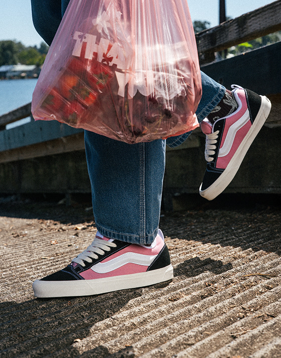 A knee-down shot of someone wearing pink and black Knu Skool with blue jeans on a boat ramp near the water.