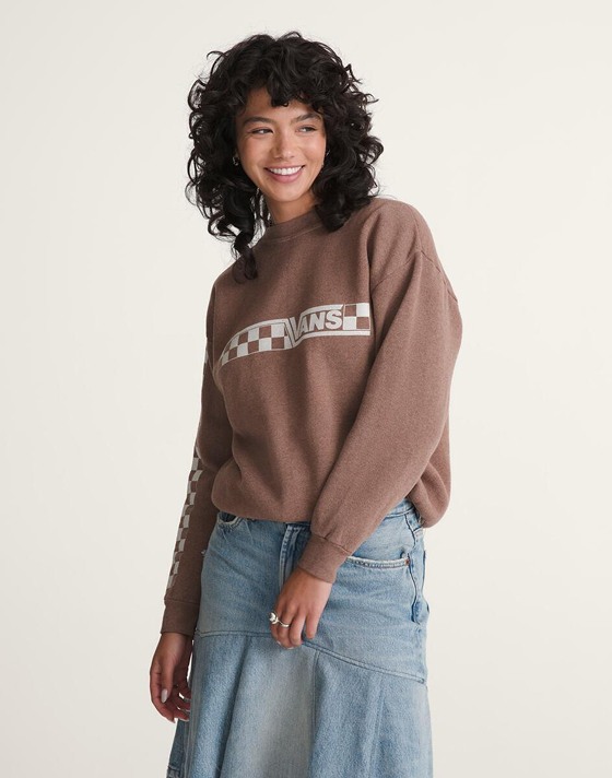 A young woman poses in a photography studio wearing a brown Vans sweater with a Checkerboard pattern.
