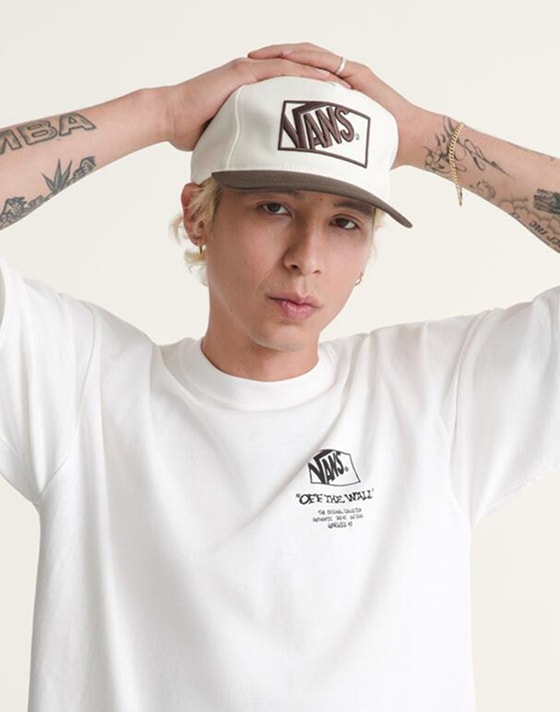 A young woman man in a photography studio wearing a brown Vans sweater with a Checkerboard pattern.