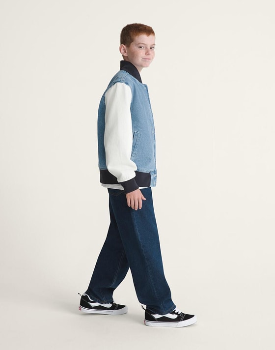 A young man poses in a photography studio wearing a blue Checkerboard tracksuit.
