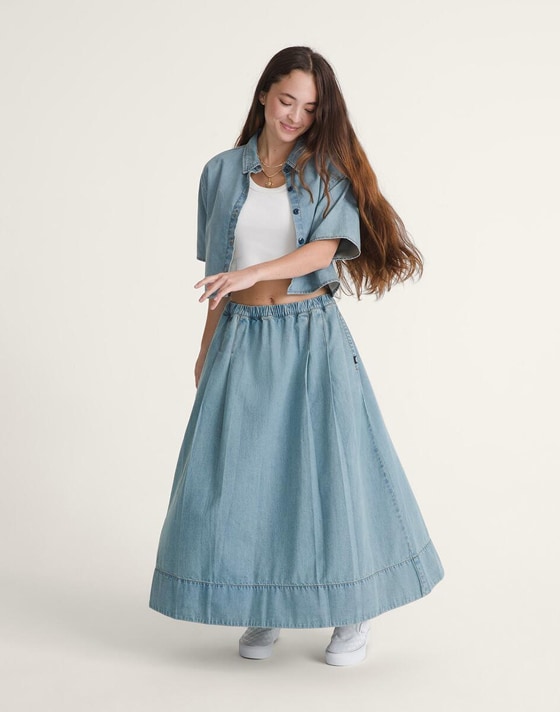 A woman twirls in a denim overshirt and skirt wearing white Authentic in a photography studio.