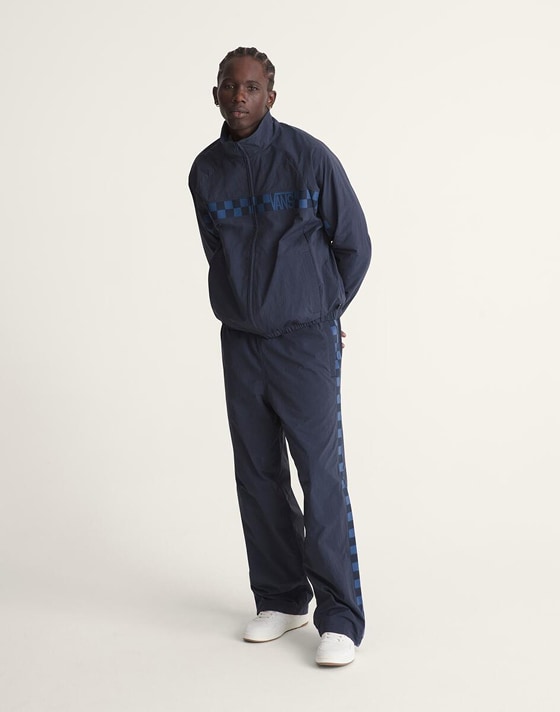 A young man poses in a photography studio wearing a blue Checkerboard tracksuit.