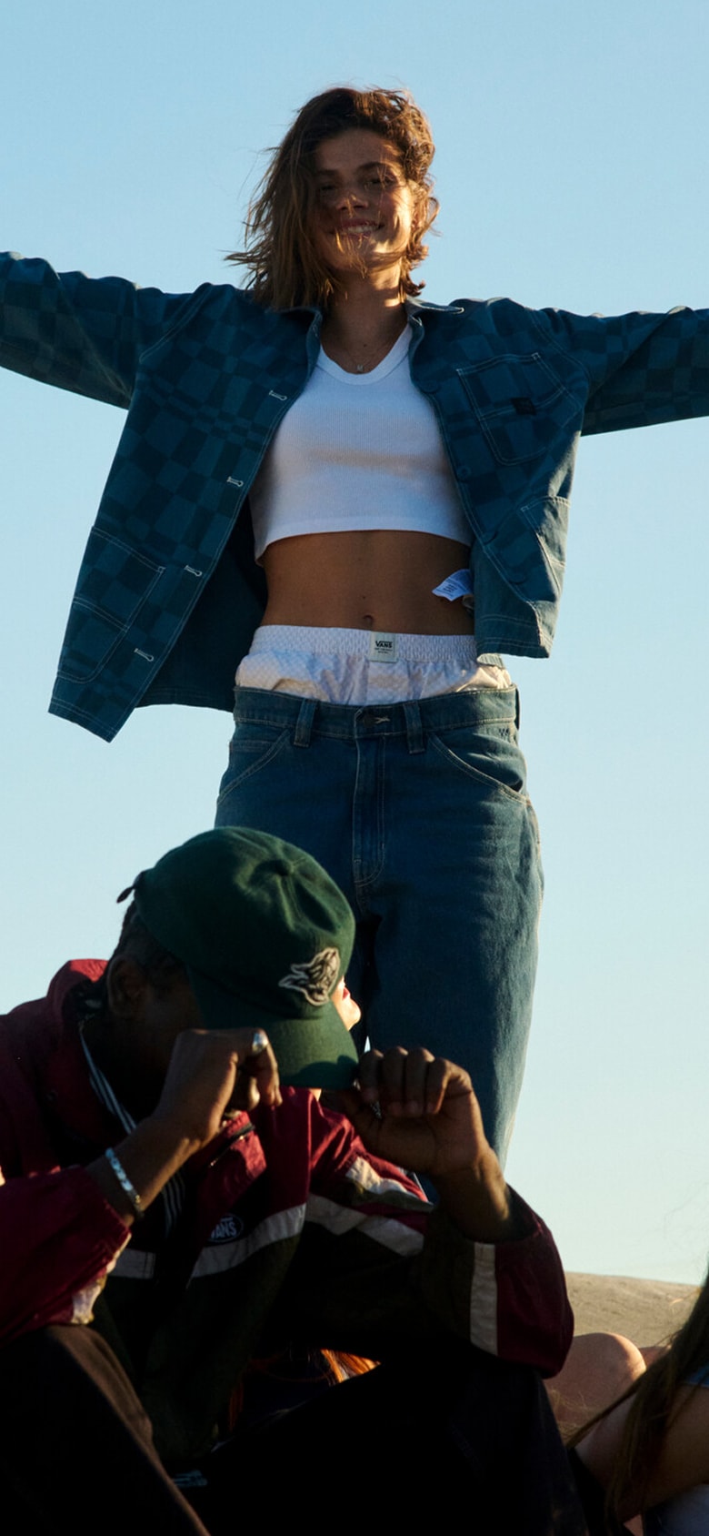 Two young women hang out and laugh on a roof wearing Vans clothes and shoes during golden hour.