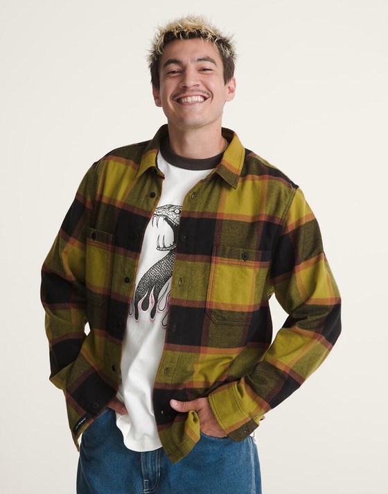 A waist-up shot of a man wearing a yellow flannel and smiling at the camera.