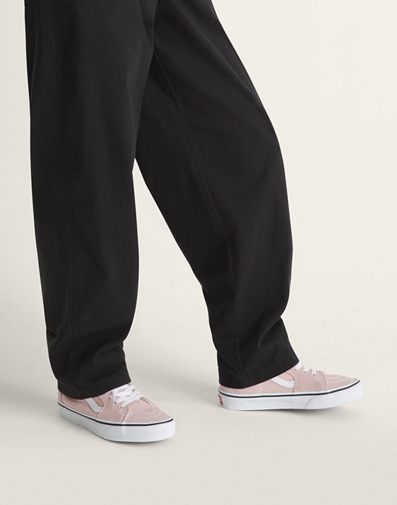 A waist-down shot of a woman wearing black sweats with pink Old Skool.