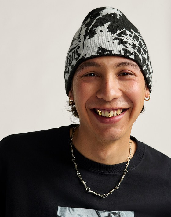 A young man smiles at the camera wearing a black and white Hovley Beanie in a photography studio.