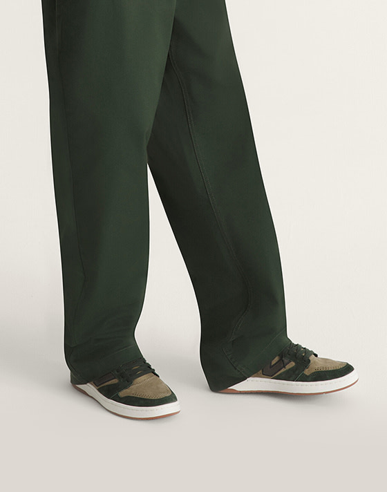 A waist-down shot of a young man wearing dark green Authentic Chino Loose pants in a photography studio.