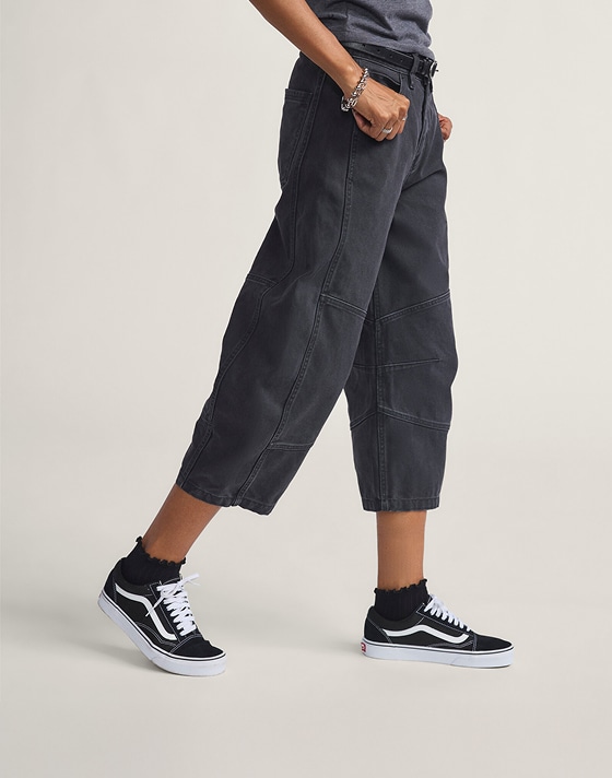 A waist-down shot of a woman wearing blue Annabelle Pants with black and white Old Skool in a photography studio.