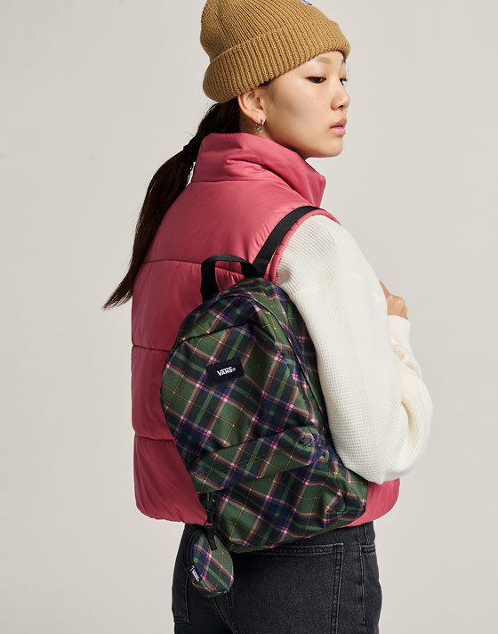 A woman poses in a photography studio wearing a mauvewood MTE Hillgate Cropped Vest and a pine forest Old Skool Mini Backpack.
