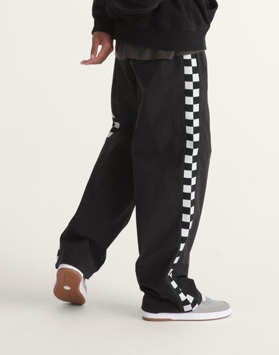 A waist-down shot of a man wearing black Checkerboard track pants.