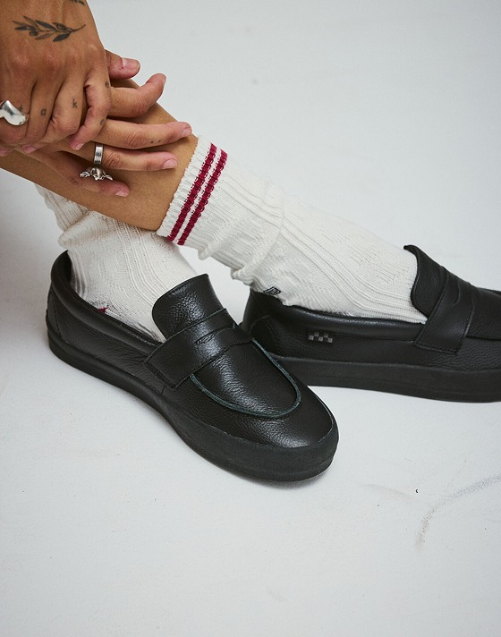 A close-up on the black Skate Loafer paired with white crew socks in a photography studio.