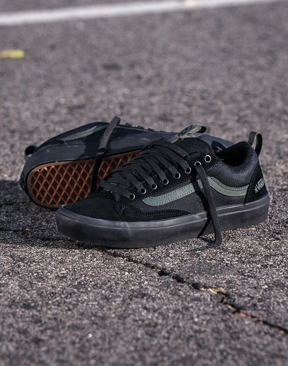 A pair of green and black Skate Old Skool 36+ lie on the blacktop from the United Through Skateboarding collection.