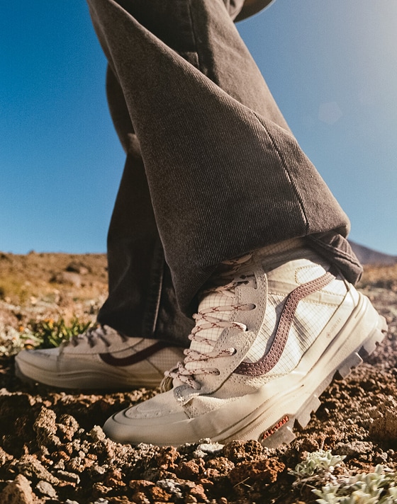 A close-up of someone wearing the red and white Sk8-Hi GORE-TEX and walking on a hillside with blue sky in the background.