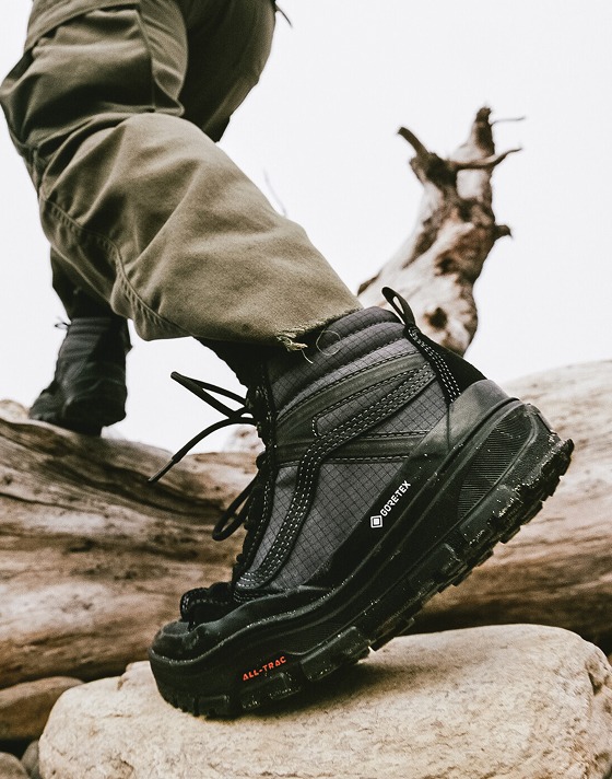 Close-up of someone wearing the black Sk8-Hi GORE-TEX walking in the woods over a log.