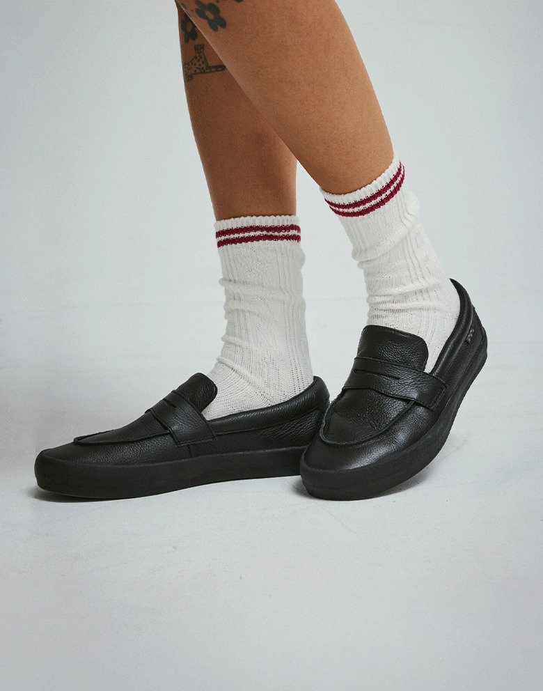 A close-up on the black Skate Loafer in a photography studio paired with white socks and blue denim jeans.