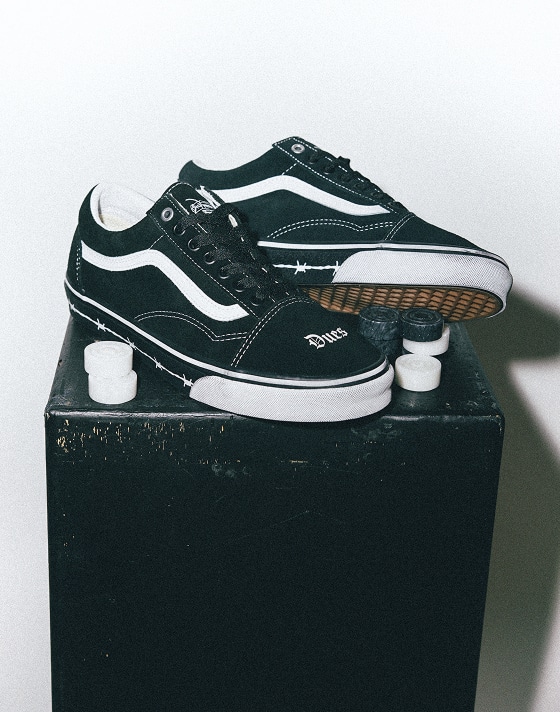 The Vans x Travis Barker Old Skool lie on top of a black wooden box in a photography studio.