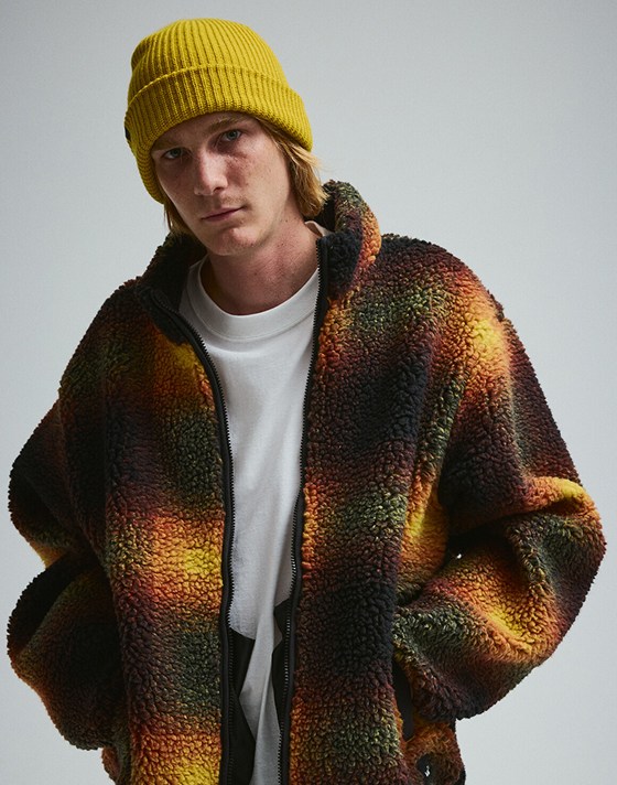 A young man wearing a High Pile Fleece Jacket and a yellow beanie in a photography studio.