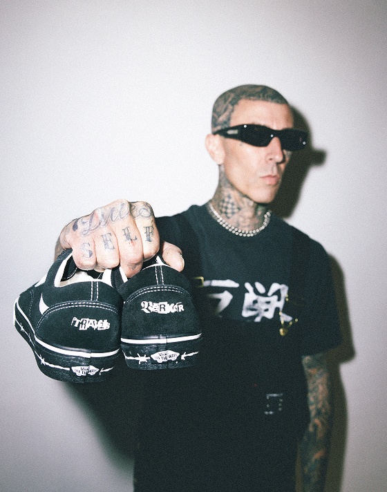 Travis Barker holds up the Vans x Travis Barker Old Skool in a photography studio with his tattooed knuckles.