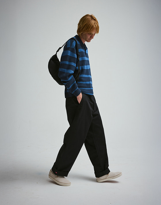 A young man walking in a photography studio wearing a blue striped polo and beige Classic Slip-On.