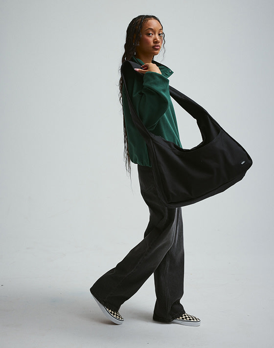 A young woman walking with a black bag and Checkerboard Classic Slip-On in a photography studio.